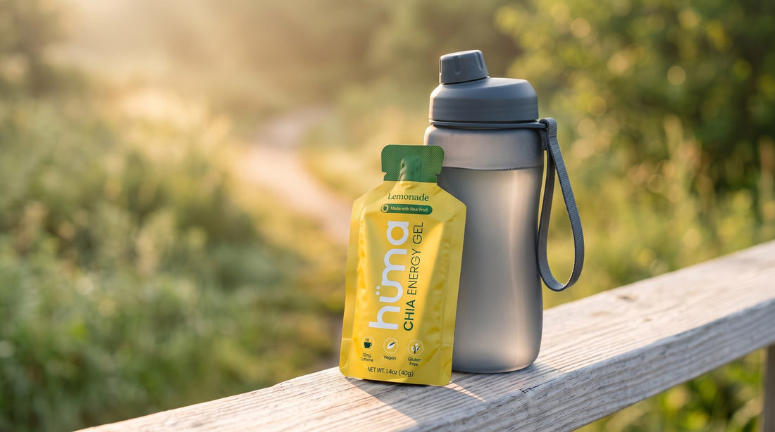 A Huma Lemonade chia energy gel leaning against a runner's handheld water bottle on a wooden rail at a sunrise trailhead