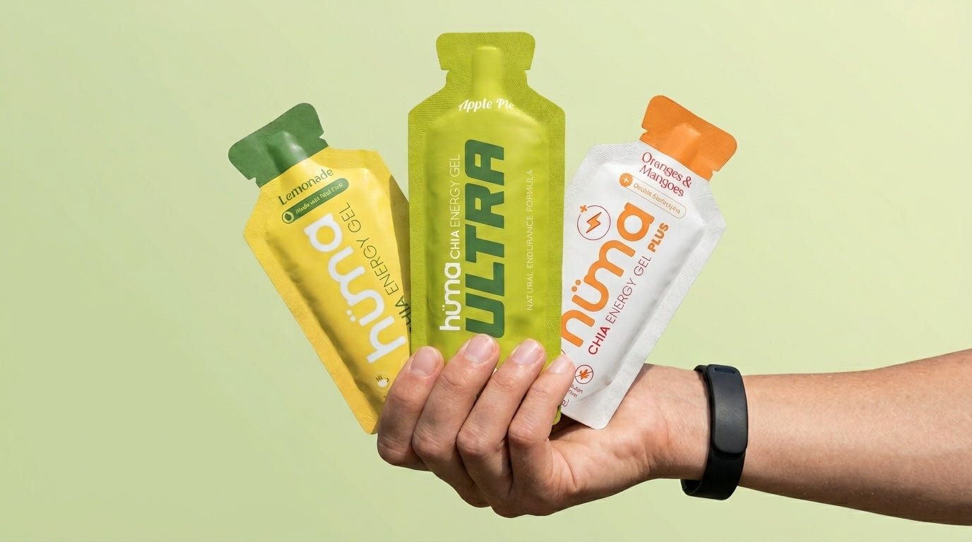 A hand holding three Huma gels - Original Lemonade, Ultra Apple Pie, and PLUS Oranges and Mangoes - against a soft pale green background